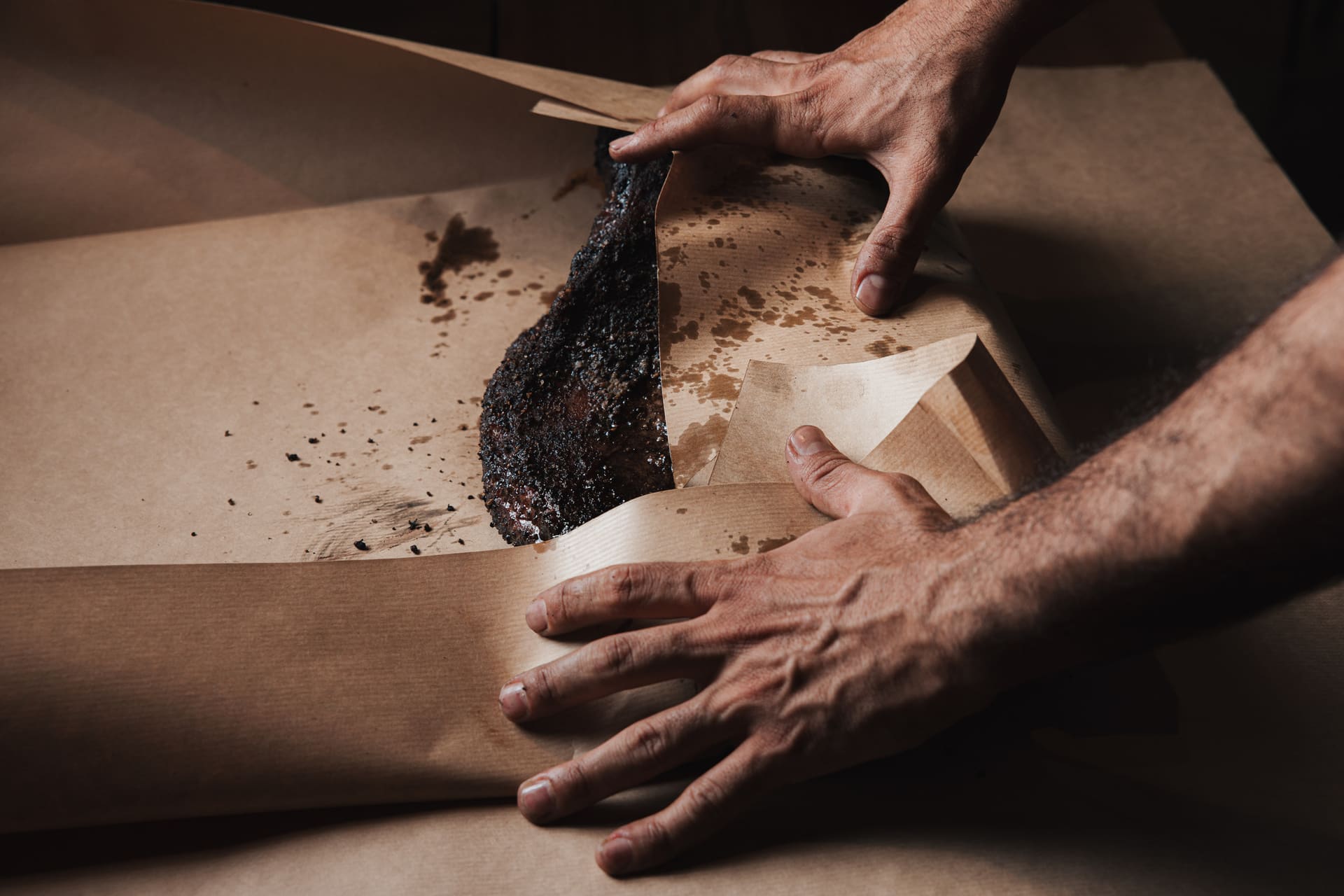 Hands wrapping a smoked brisket in butcher paper