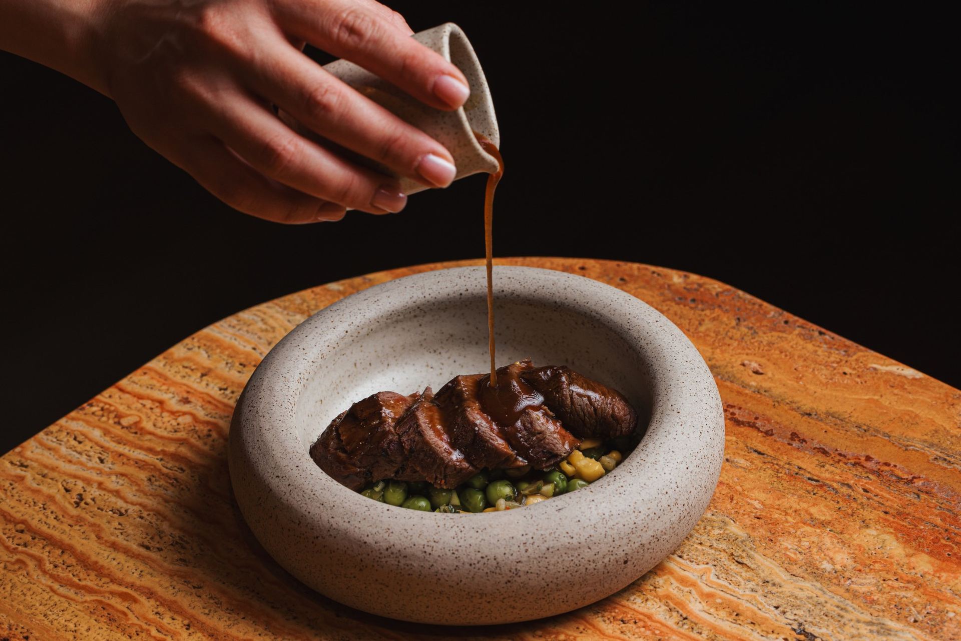Sliced smoked beef in a stone bowl, jus poured over peas and corn