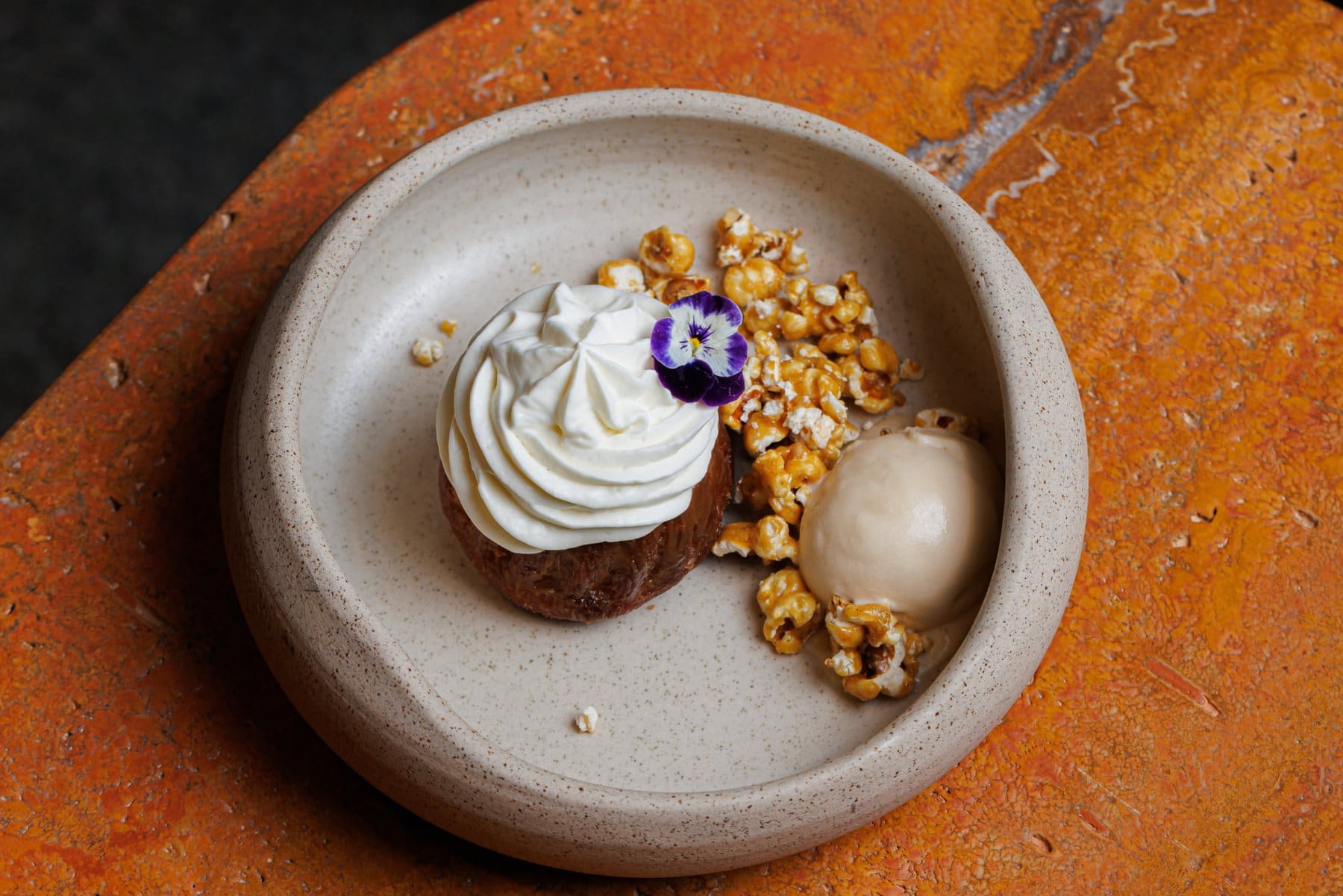 A dessert with whipped cream, caramel popcorn and ice cream on stone