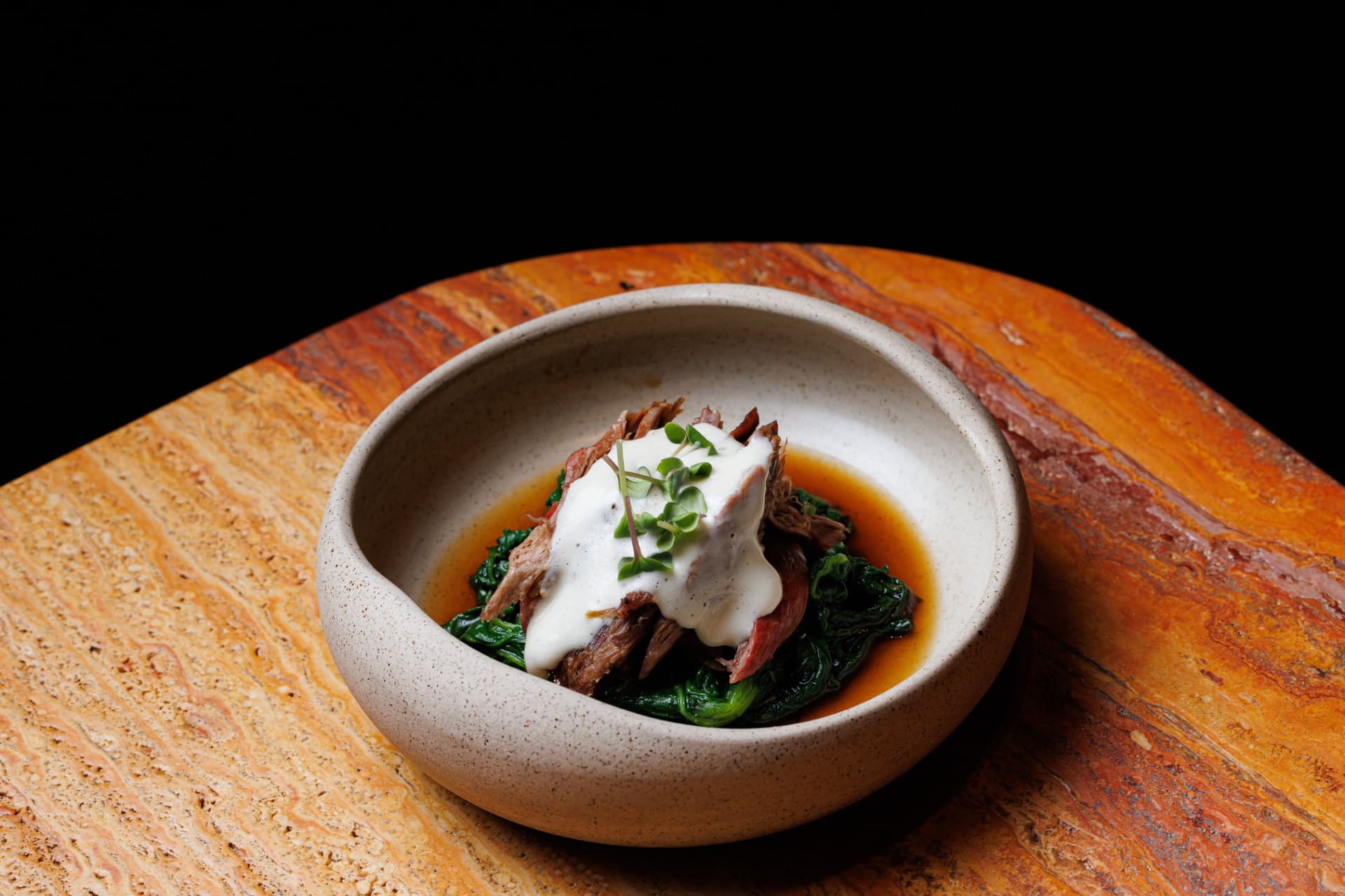 Pulled smoked meat over wilted greens in a stone bowl