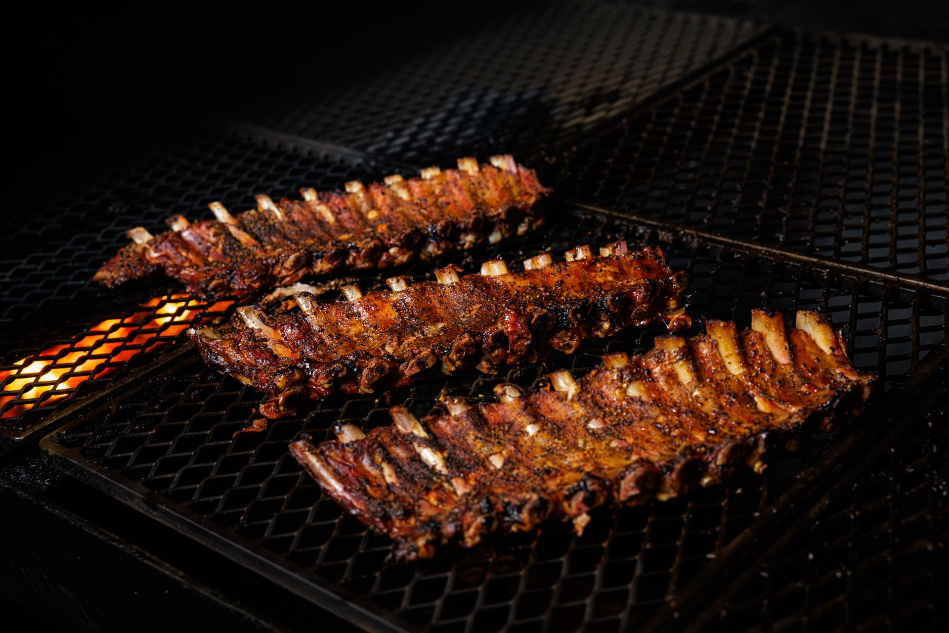 Racks of ribs in an open smoker, smoke rising from the grate
