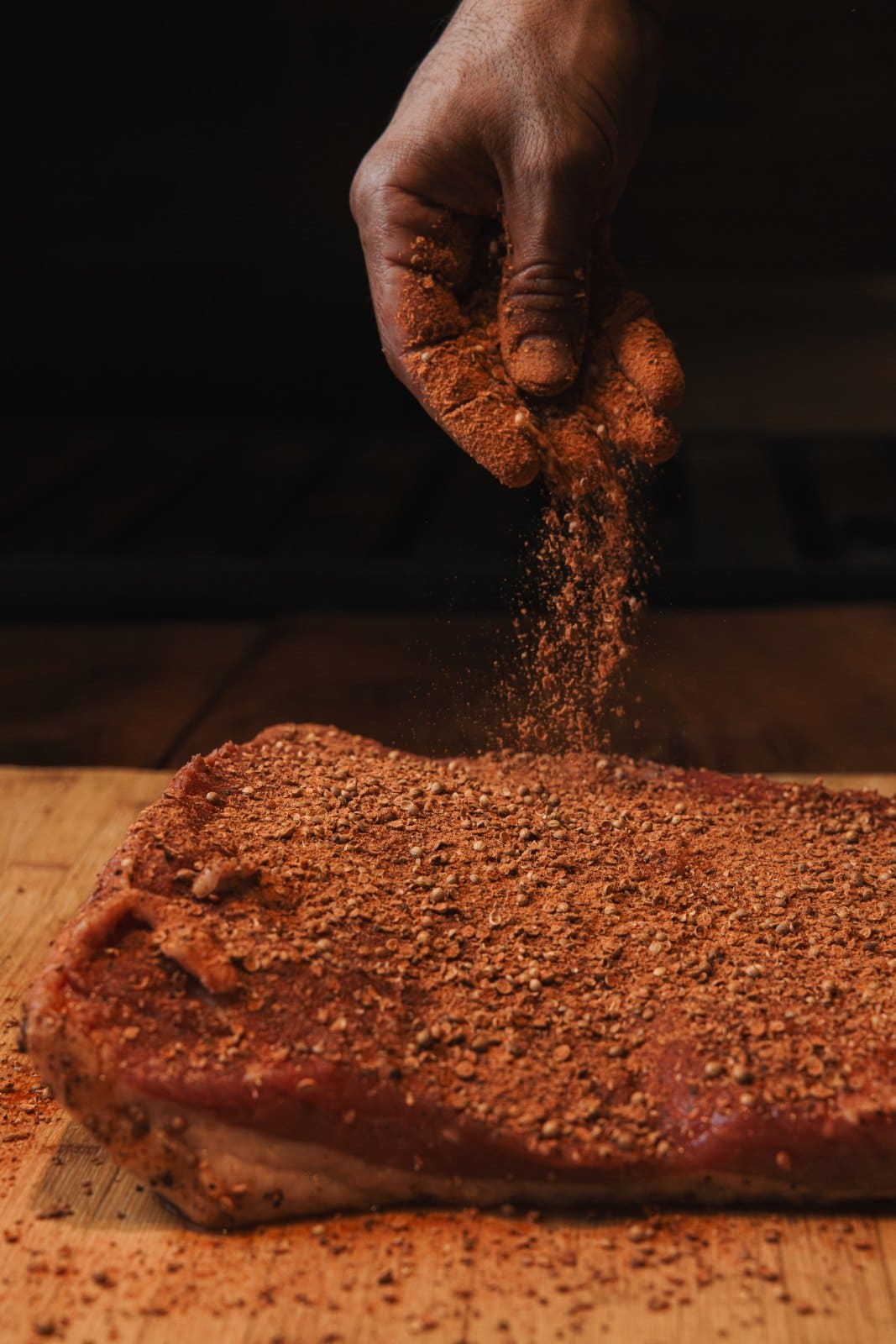 A cook dusting rub over a brisket on the board