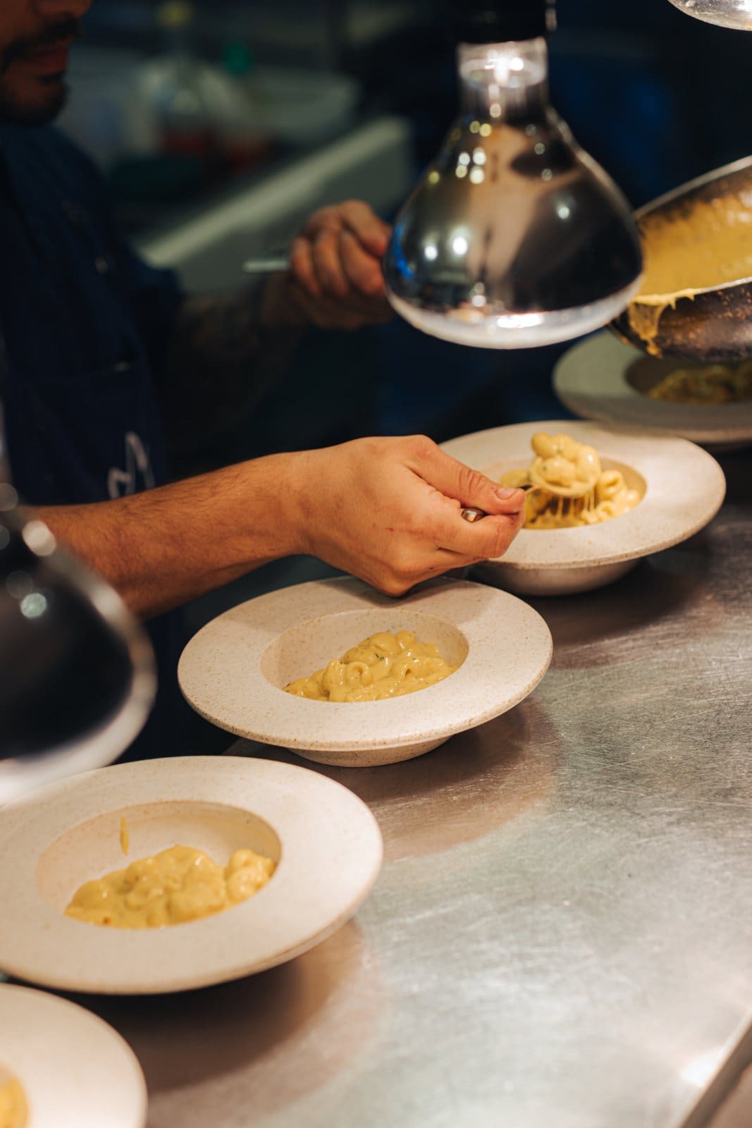A cook finishing bowls of macaroni under the pass lamp